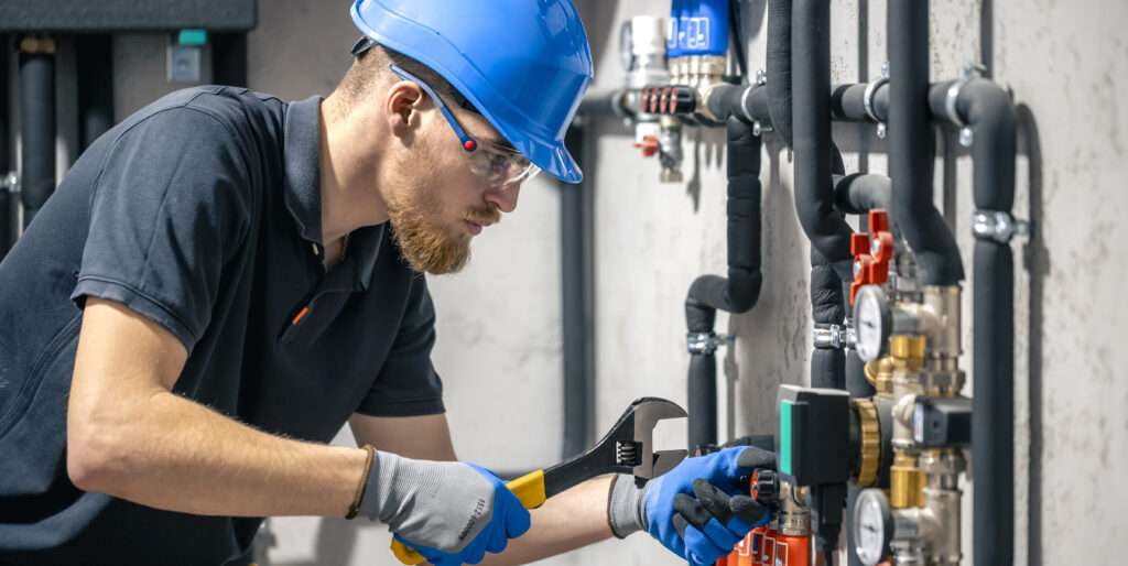man installs heating system house checks pipes with wrench scaled